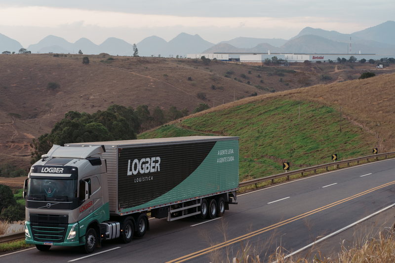 Caminhão da Logber em estrada, com a unidade ao fundo