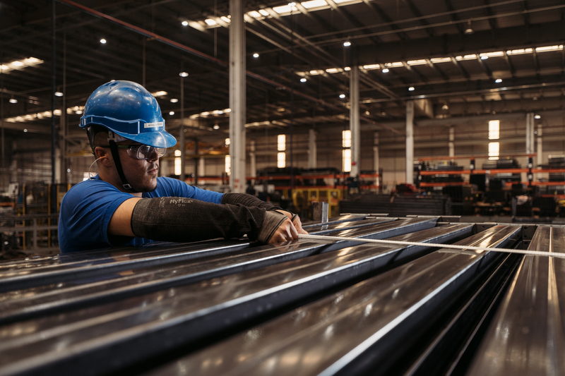 Operário conduzindo perfis metálicos em uma linha de produção
